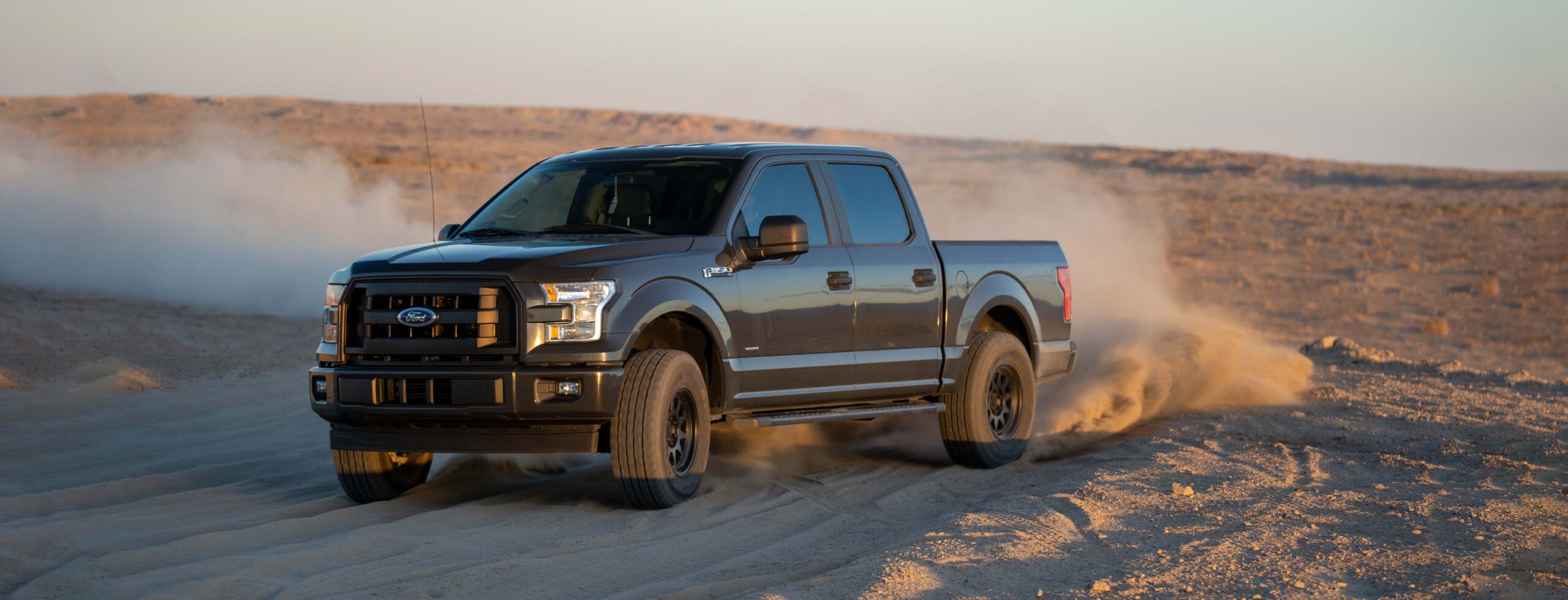 Black SUV in sandy terrain leaves dust cloud